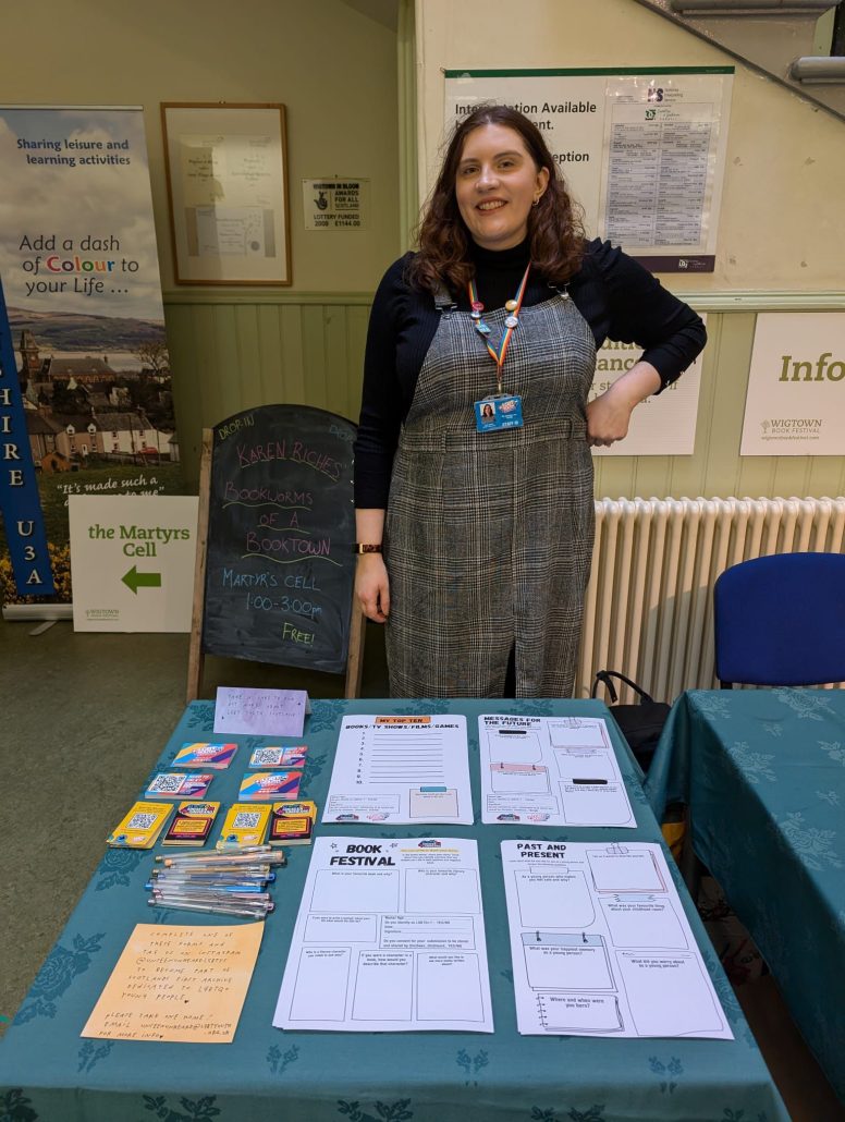 A person smiling in front of a table of worksheets.